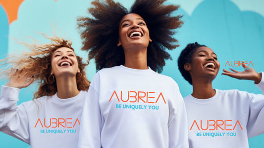 Joyful group of diverse women laughing and celebrating in unity, dressed in Aubriea's signature white sweatshirts with the uplifting slogan 'Be Uniquely You' emblazoned in orange. 